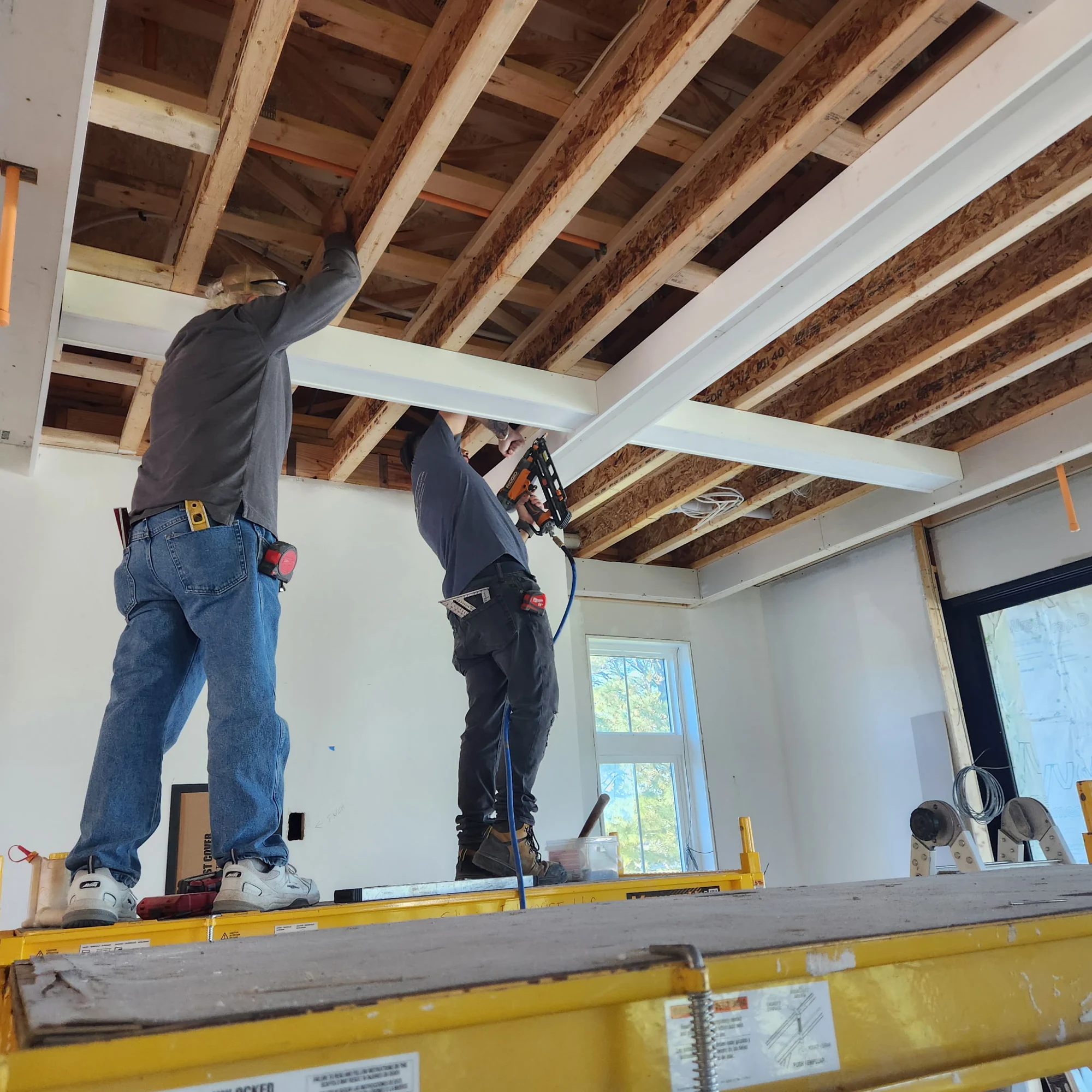 Two people working beneath exposed wood ceiling framing on site