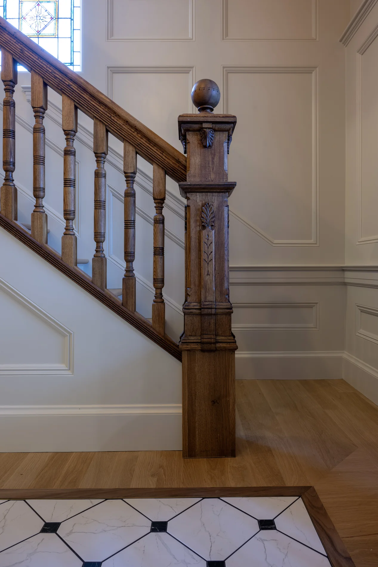 Wood newel and turned balusters beside painted wall paneling