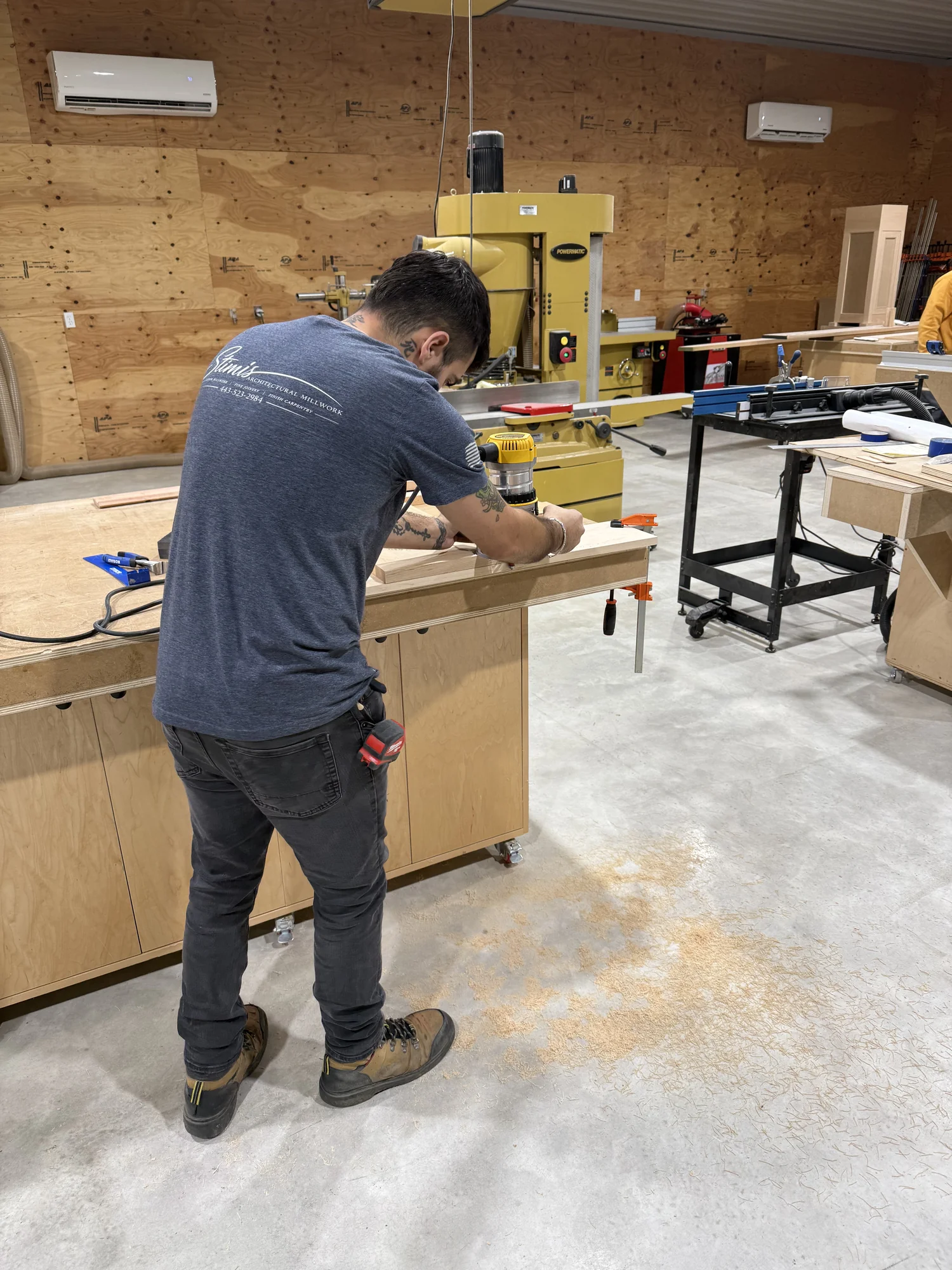 Stimis apprentice working with handheld router at a timber workbench in the fabrication shop.