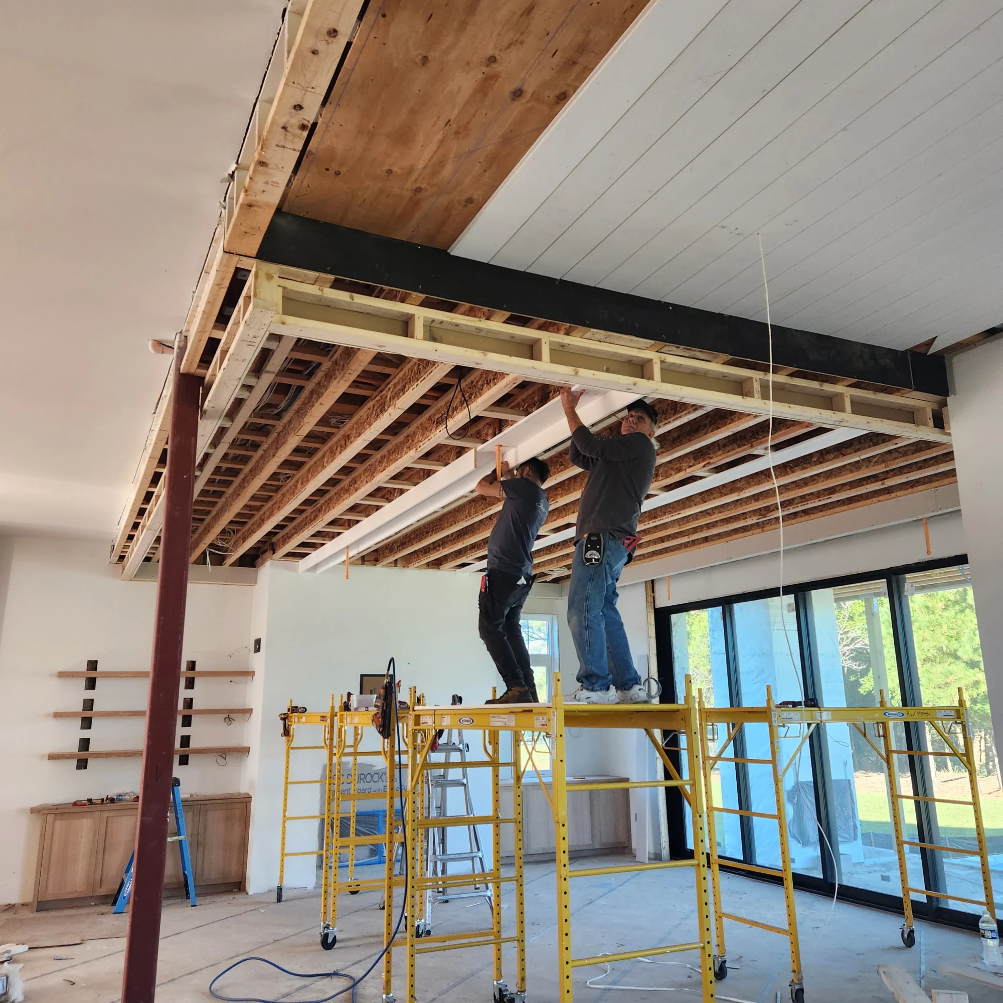 Two people on staging working beneath an unfinished wood ceiling on site
