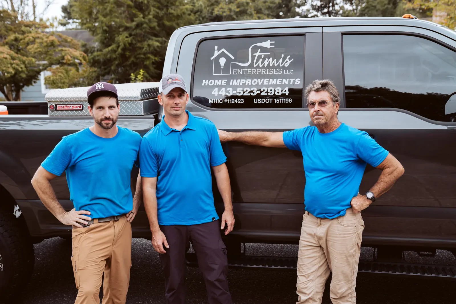Three members of the Stimis team in matching blue shirts beside a company truck