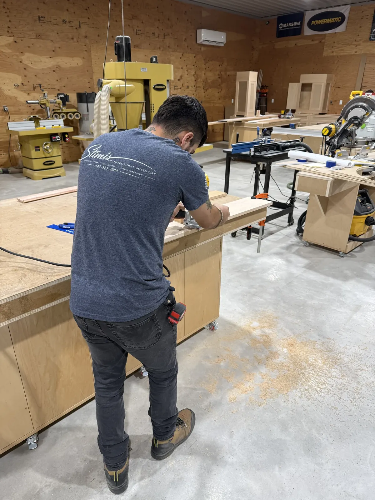 Stimis apprentice working with handheld router at a timber workbench in the fabrication shop.